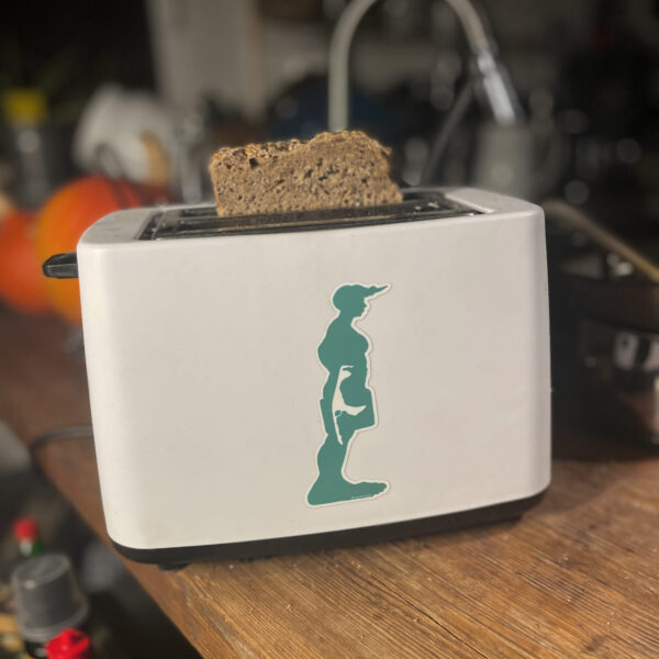 Der Insel Sylt Aufkleber von Neptunsgeschmeide, mit grüner Riesin als Motiv klebt auf einem Toaster. Hintergrund zeigt eine Küche in Norddeutschland.